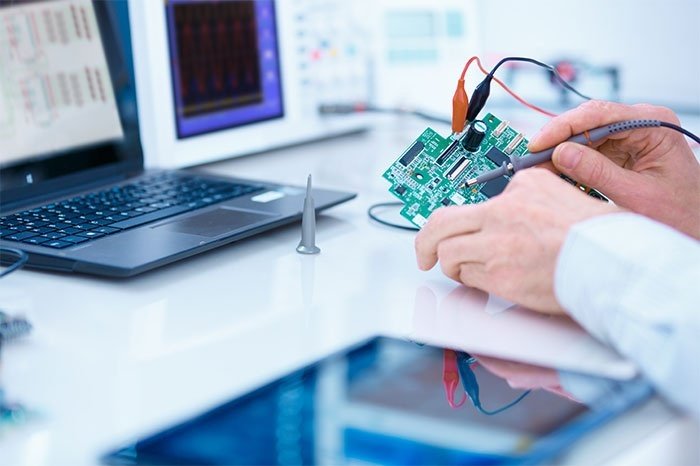 Technician holding a circuit board in front of a laptop Technician holding a circuit board in front of a laptop